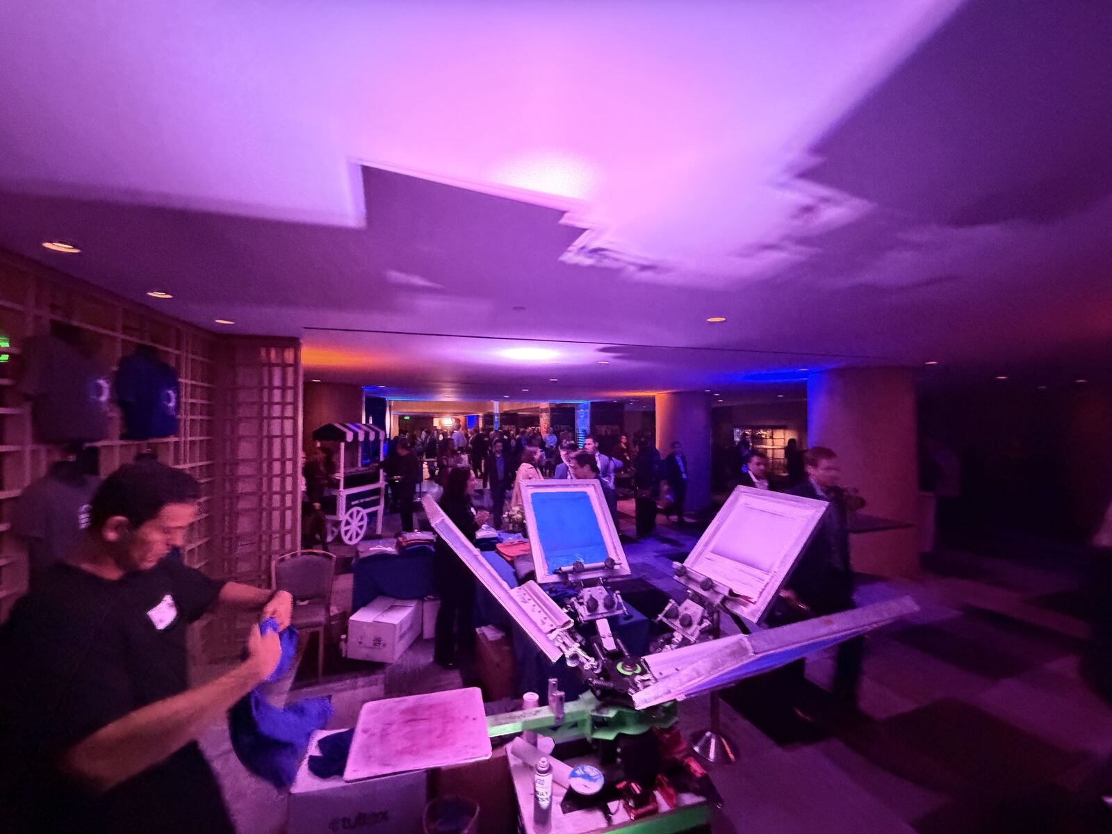 Live event booth with heat press stations displaying decorated apparel to attendees in a purple-lit venue