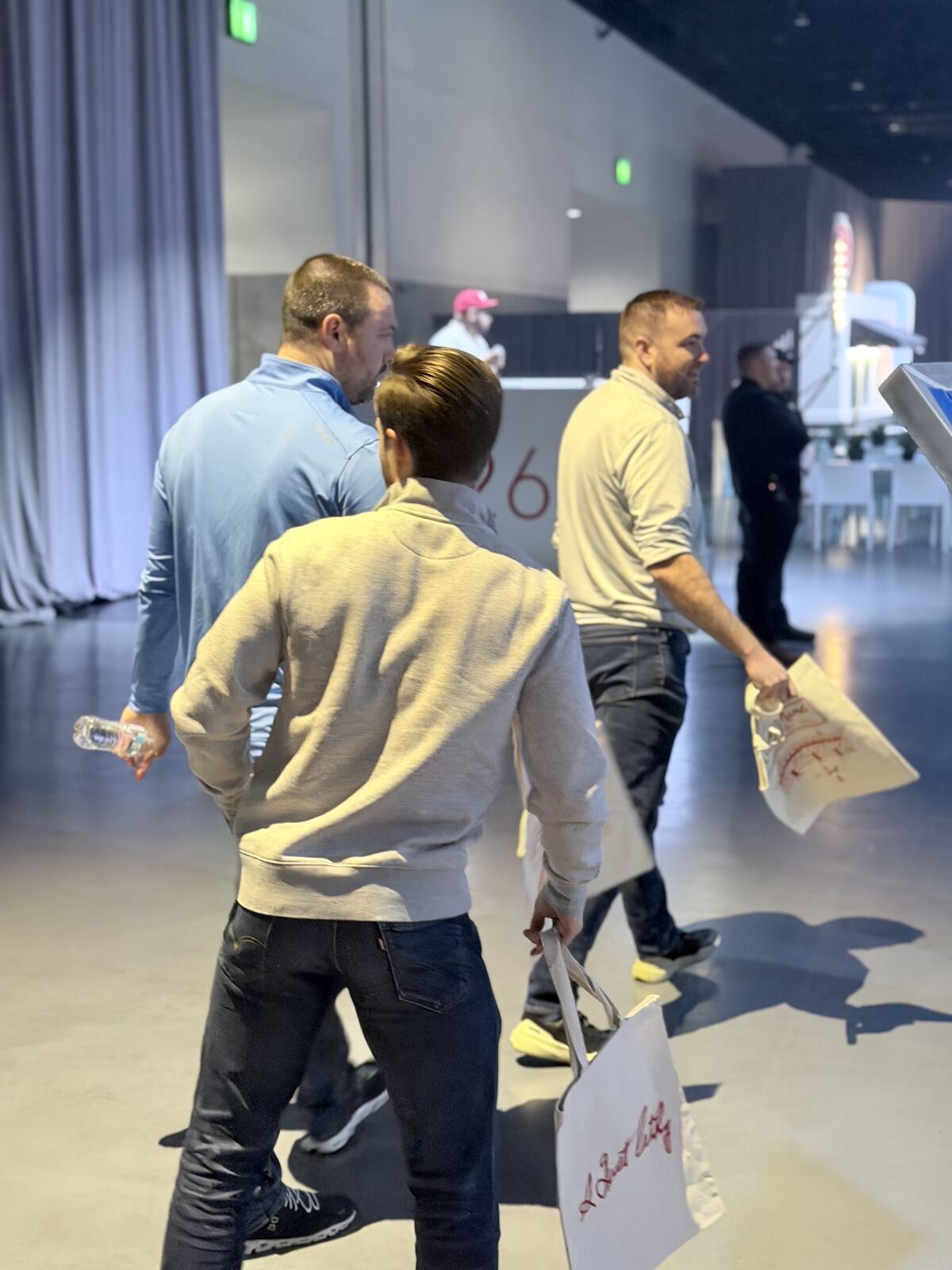 Three attendees examining and holding printed materials at an indoor event booth with controlled lighting